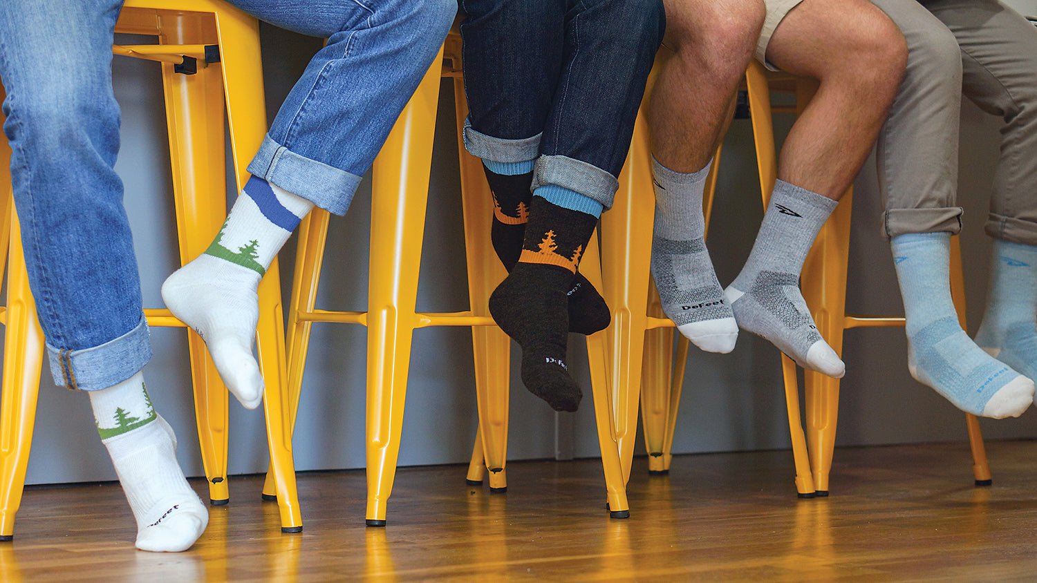 DeFeet Woolie Boolie socks in a variety of styles worn by people sitting on tall stools